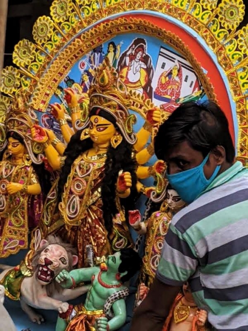 Chandreyee Chatterjee's family brings home a smaller Durga this year, Kolkata, India. A man holds an ornate Durga idol in his arms while he wears a mask