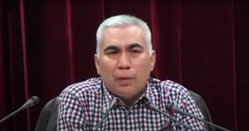 Abduqadir Jalalidin speaks into a microphone A man with silver hair speaks into a microphone wearing a plaid, button-down shirt