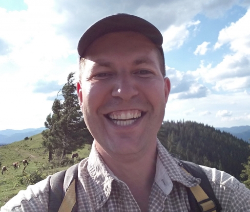 A selfie of Andriy Gnytka. A selfie of Andriy Gnytka, a white man wearing a hat and smiling in the sunshine with his backpack on his back and trees behind him