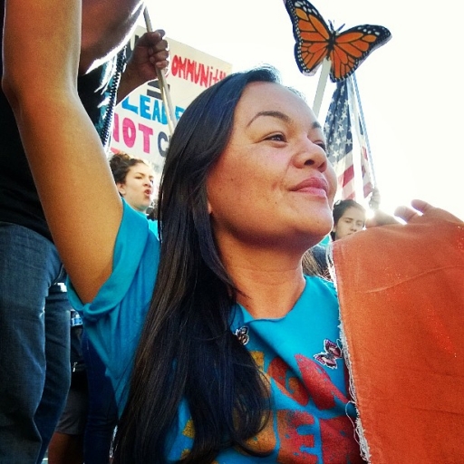 Francisca Porchas is the founder of the Latinx Therapist Action Network. Her work was inspired by the experiences of activists advocating in immigrant communities and the emotional toll that it took on them. A woman wearing a blue shirt stands with a hand up and a monarch butterfly image near her.