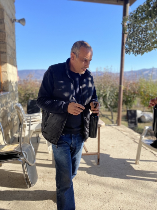 A man holds a wine bottle outside under a blue sky. 