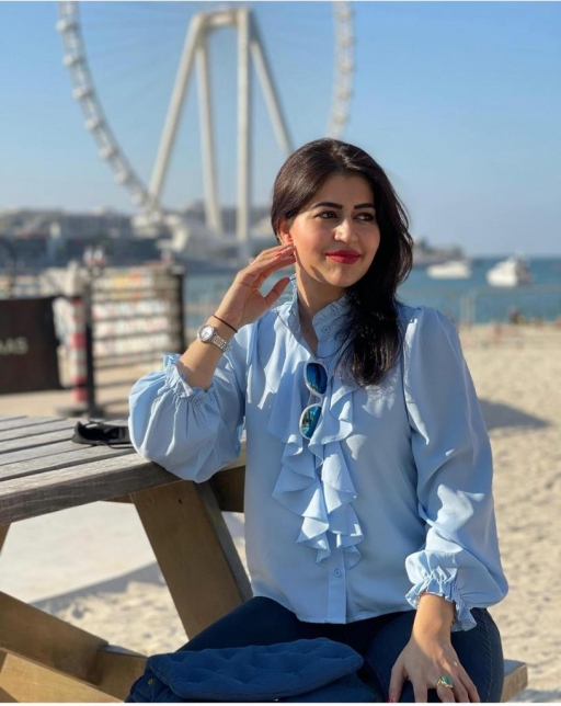 Birmingham general practitioner Dr. Anita Raja is acutely aware of vaccine hesitancy in her patients. A woman wearing a blue top and jeans poses on a bench outdoors in front of a Ferris wheel.