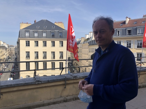 Denis Gravouil, a cinematographer and head of the CGT Spectacle Trade Union, stands on the balcony of the Odeon Theater. Gravouil is one of 42 people who have been illegally occupying the building since early March. A man stands holding a mask on a theater balcony over looking a plaza.