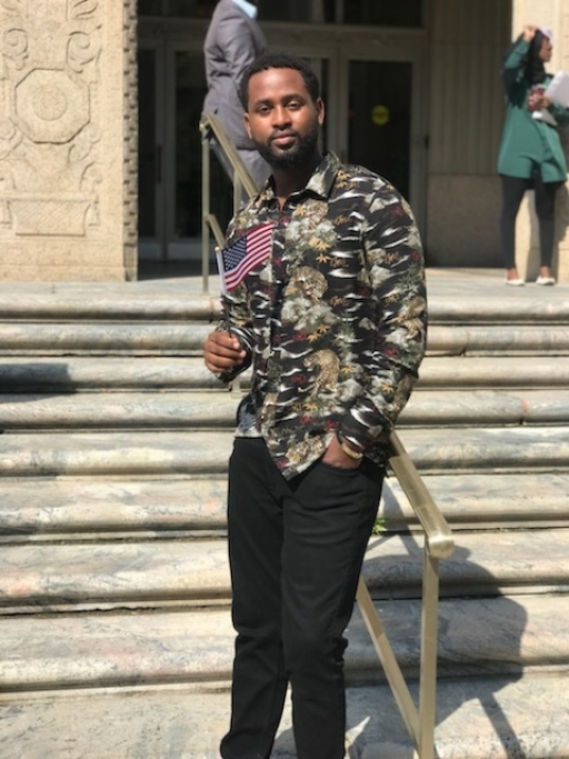 Young man from DR Congo stands on a set of steps holding a mini-American flag.