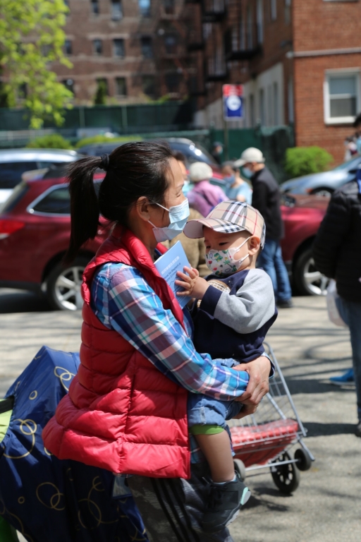 Asian Americans benefit from a booklet on "How to Report a Hate Crime" Woman wearing blue and red carries a child who is flipping through a booklet on "How to Report a Hate Crime"