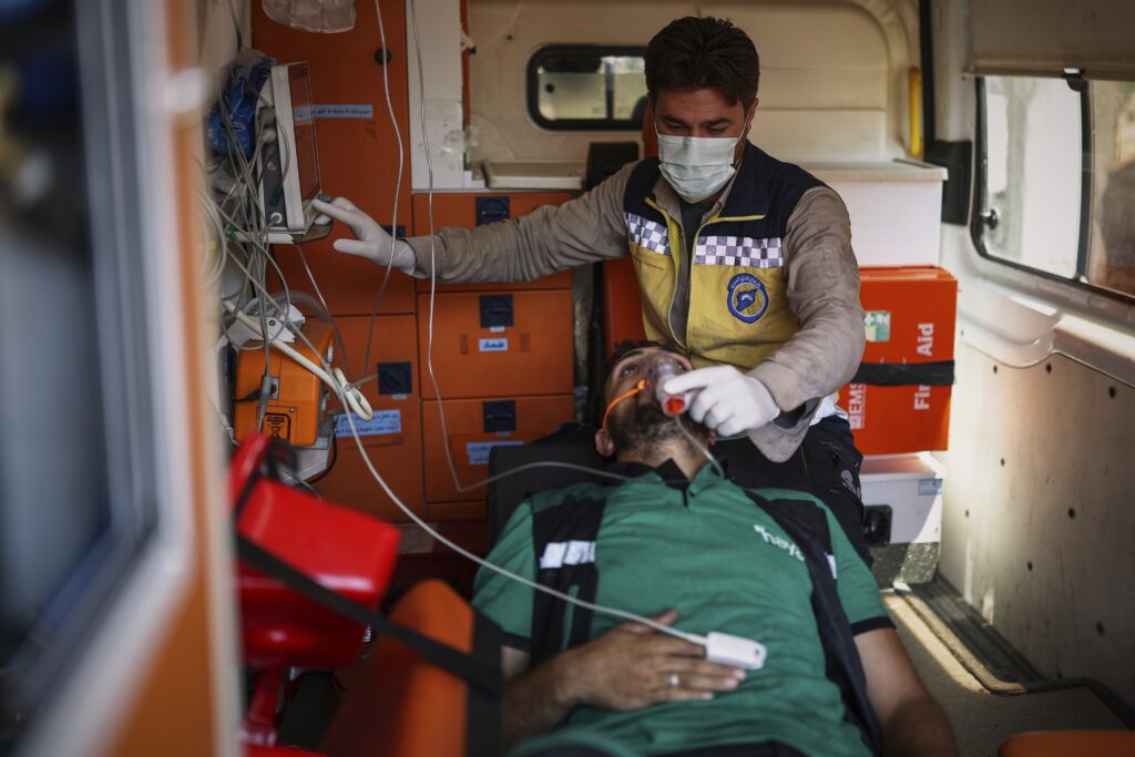 A paramedic wearing a mask and gloves is attending to a patient inside an ambulance, monitoring his vital signs and adjusting medical equipment.