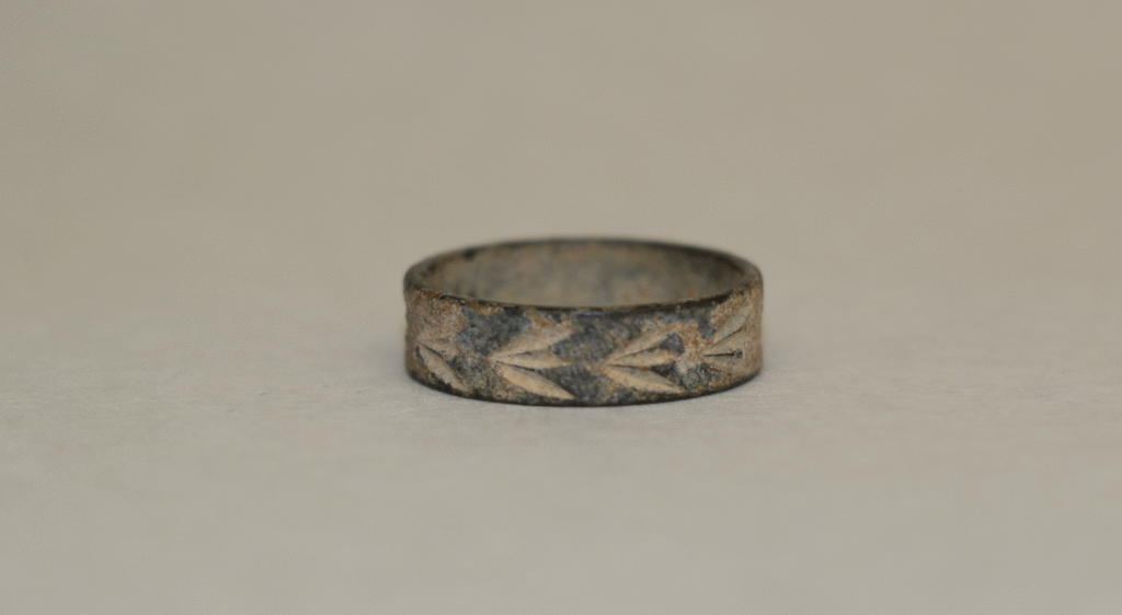 A bronze ring with a simple leaf pattern design engraved around its band, set against a plain background.