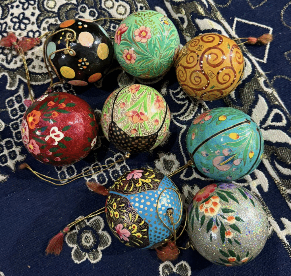 A collection of colorful, hand-painted decorative balls with floral and abstract patterns, displayed on a blue patterned fabric background.