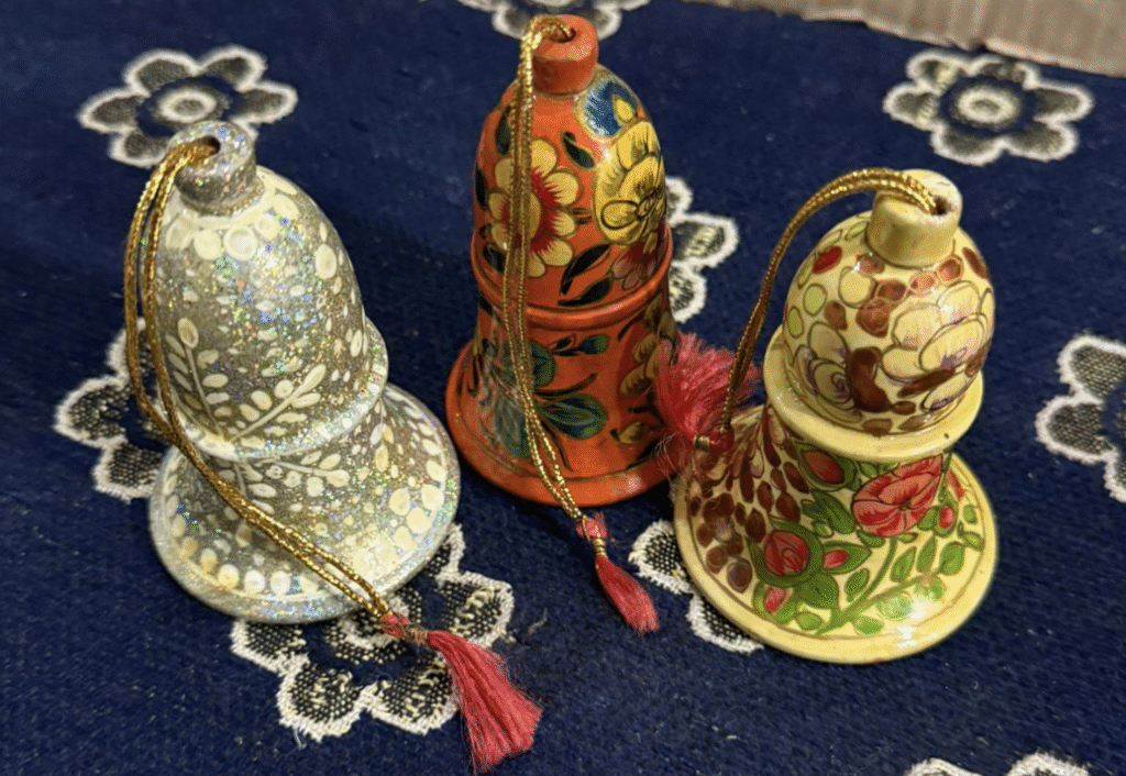 Three intricately decorated bell-shaped ornaments with floral designs and tassels, placed on a blue fabric with white patterns.