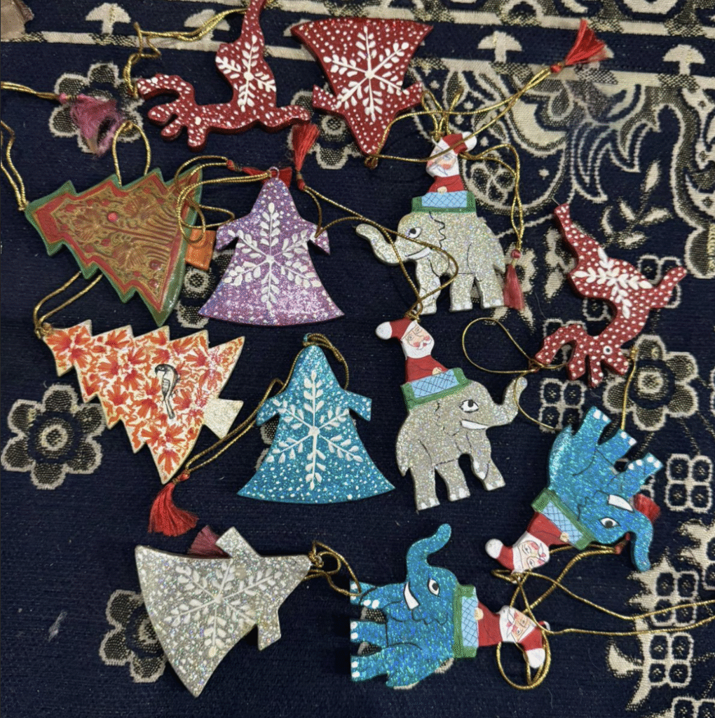 A collection of colorful Christmas tree ornaments featuring elephants, trees, and reindeer shapes, decorated with snowflake patterns and glitter, lying on a dark patterned fabric.