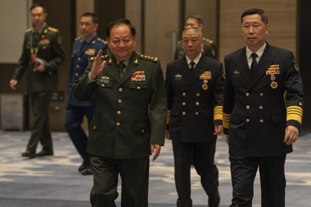 A group of military officials in uniform walking indoors, with visible medals and insignia on their attire.