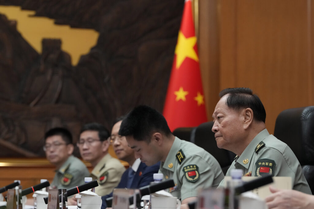 Chinese military officials in uniform sit in a meeting with a Chinese flag in the background.