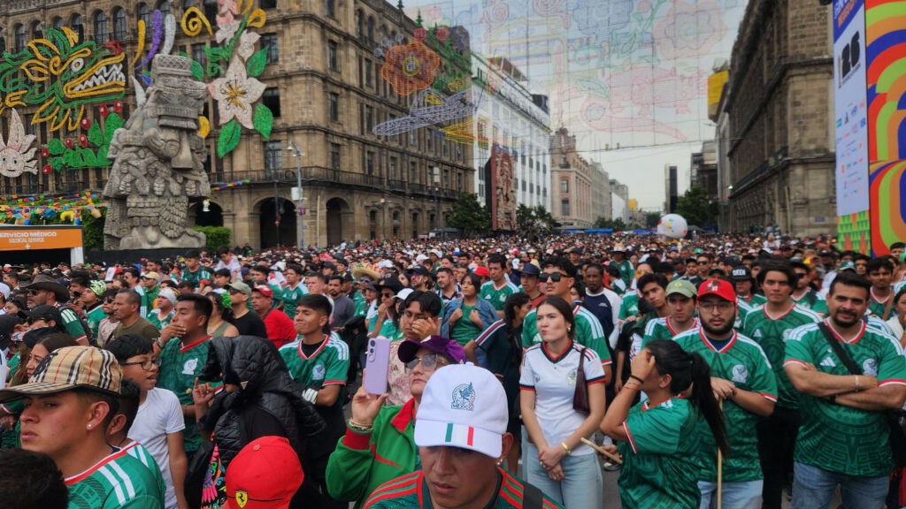 Large crowd of Mexico soccer fans in green national team jerseys gathered outdoors in Mexico City's Zócalo plaza