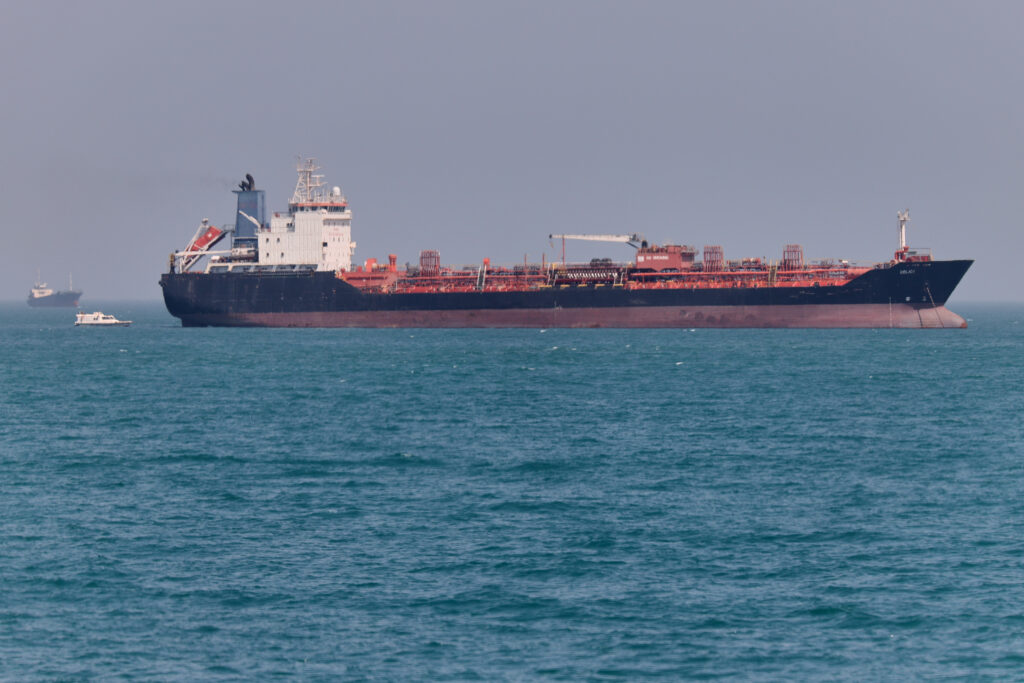 Large oil tanker anchored at sea with a small boat nearby under a hazy sky