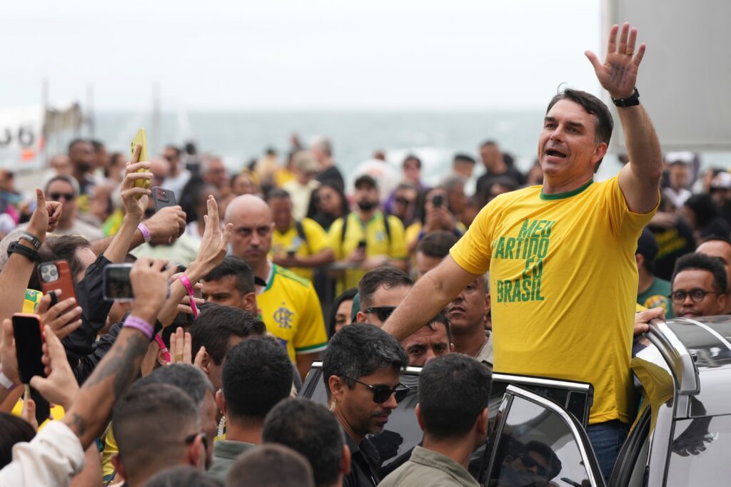 Jair Bolsonaro waves to a large crowd of supporters, wearing a yellow shirt reading