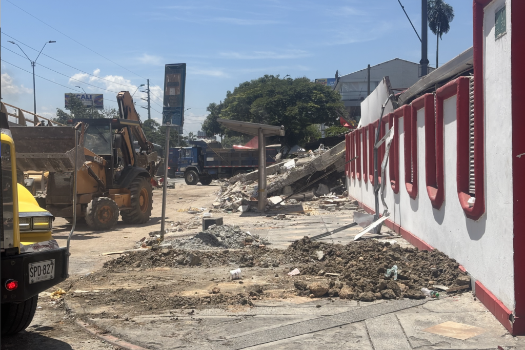 A backhoe and dump truck clear rubble and collapsed concrete structures from a demolition site in Cali, Colombia