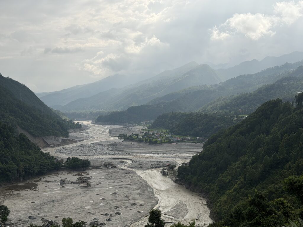 Mountain valley river flooded with sediment, submerging buildings amid debris near the water's edge