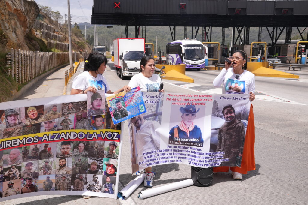 Women hold banners and posters at a highway tollbooth demanding answers on Colombian men missing in Ukraine, banner reads 