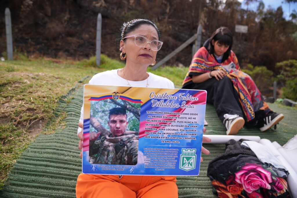Woman holds memorial plaque for Cristhian Fabian Villalobos Susa, a soldier, with a tribute message reading she misses him deeply and will never forget him