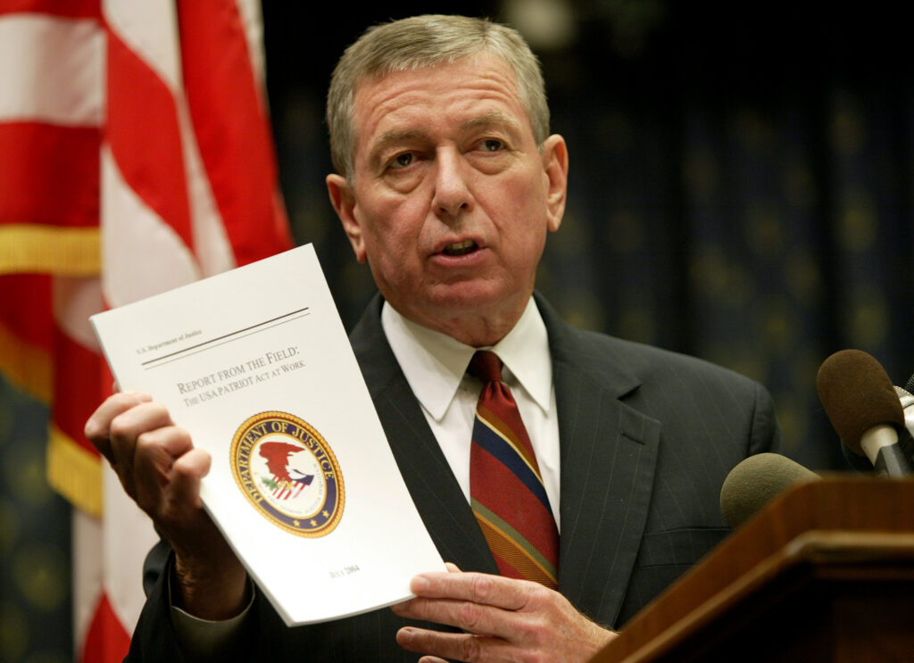 Man at podium holds up Justice Department report titled 