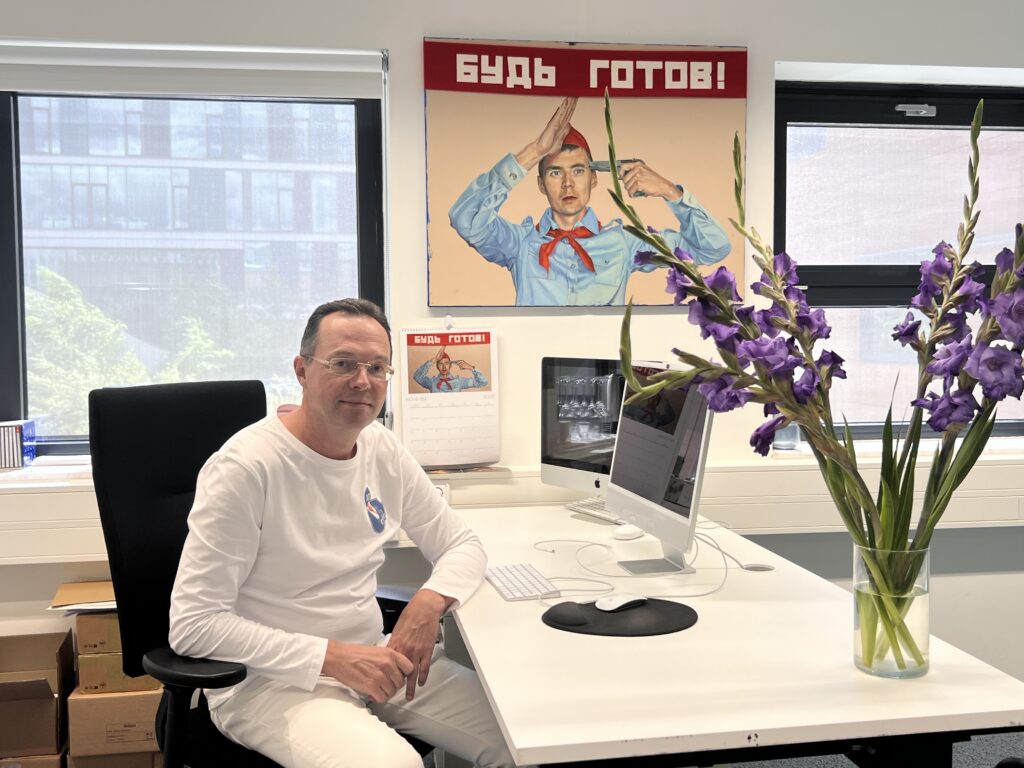 Мужчина за белым столом с iMac и фиолетовыми цветами гладиолусов, подпись: "Готово!" показано, как пионер отдает честь, приставив к голове пистолет, рядом находится соответствующее изображение календаря.