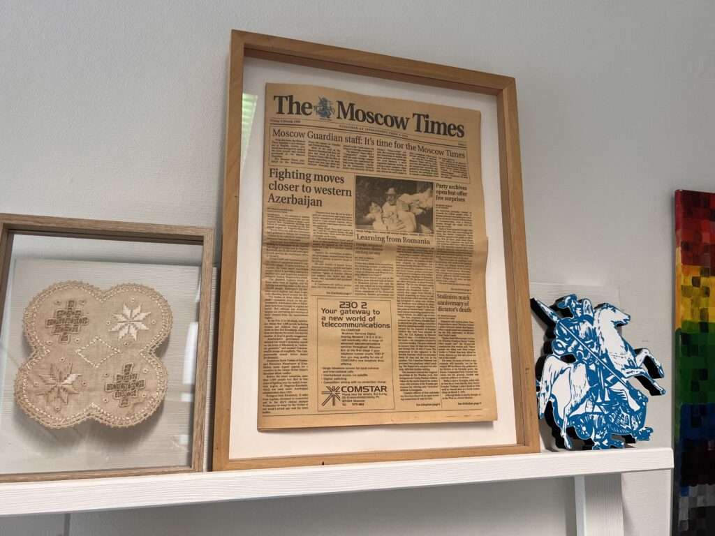 Первый номер The Moscow Times в рамке, датированный пятницей, 6 марта 1992 года, стоит на полке рядом с кружевной вышивкой и синей гравюрой на дереве с изображением конного рыцаря.
